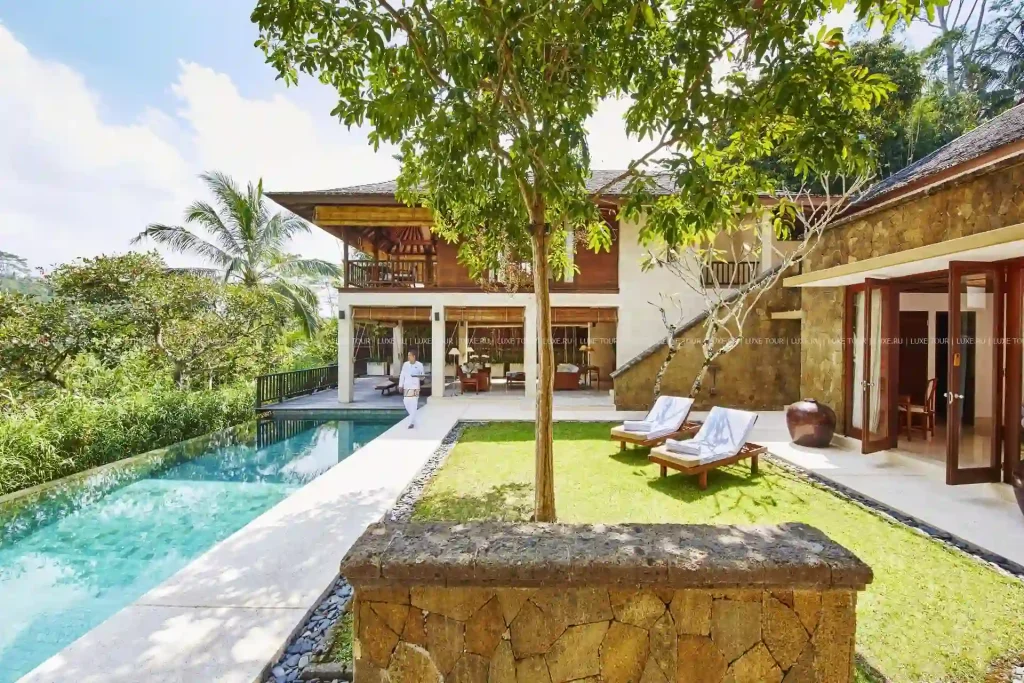 18 Cool 40th Birthday Travel Ideas (with Friends & Family) 8 A tropical villa with a Santa Fe touch features a spacious yard with sun loungers, a large swimming pool, and lush green surroundings. The villa has two stories, an open-plan design on the ground floor, and a balcony on the upper level. Trees and plants provide a serene atmosphere.