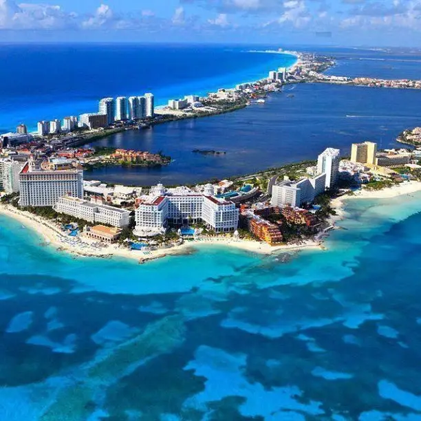 20 Bucket-List Worthy Exotic Travel Destinations to Visit Now 5 Aerial view of Cancun, Mexico, a coastal city with high-rise buildings and a mix of sandy beaches and turquoise waters. The city extends along the shoreline, blending urban structures with natural elements. The ocean showcases various shades of blue and green, epitomizing vibrant coastal beauty.