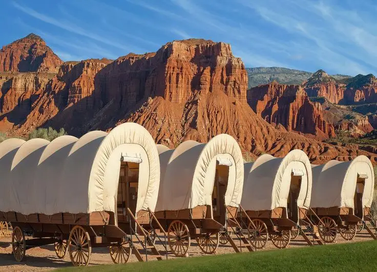 Conestoga wagons lined up in front of the majestic red rock cliffs of Capitol Reef under a clear blue sky.