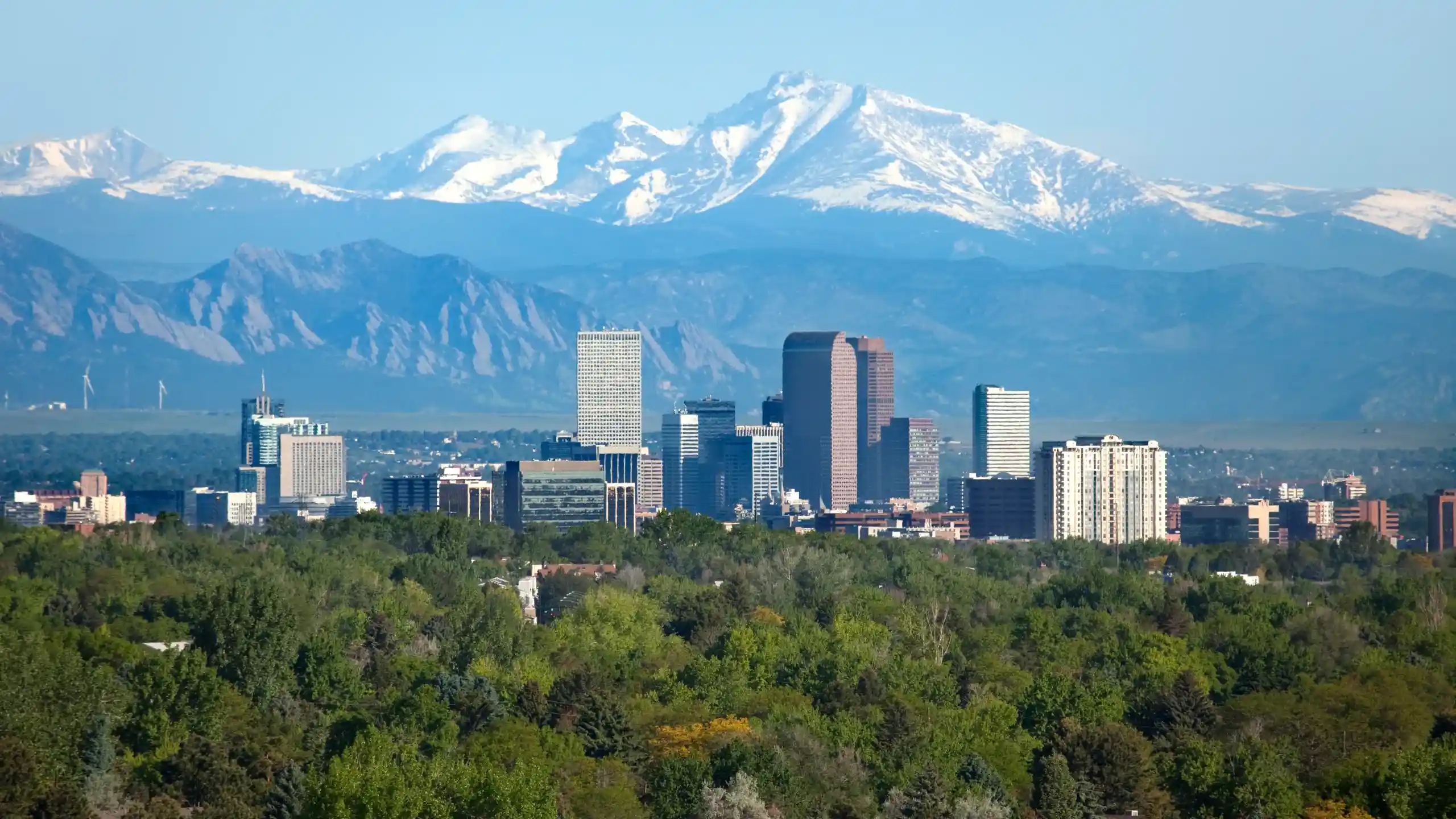 Top 10 Greenest Cities in the U.S. You Should Visit 5 The Denver city skyline, with its tall buildings, stands majestically against a backdrop of Colorado's snow-capped mountains. Green trees grace the foreground, and the sky is clear and blue.