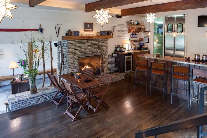 The Romantic Guide to Spoon Mountain Glamping for Beginners 14 Cozy room with a stone fireplace, wooden dining set, bar with stools, star-shaped lights, and modern kitchen reminiscent of the charming ambiance found at Jobell Cafe & Bistro.