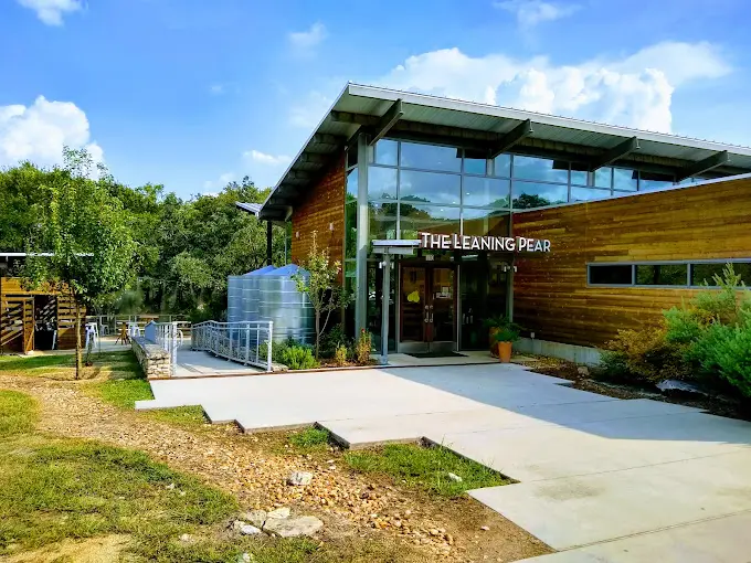 The Romantic Guide to Spoon Mountain Glamping for Beginners 11 A modern building with large windows and a sign that reads "The Leaning Pear," nestled among lush greenery under a vibrant blue sky.