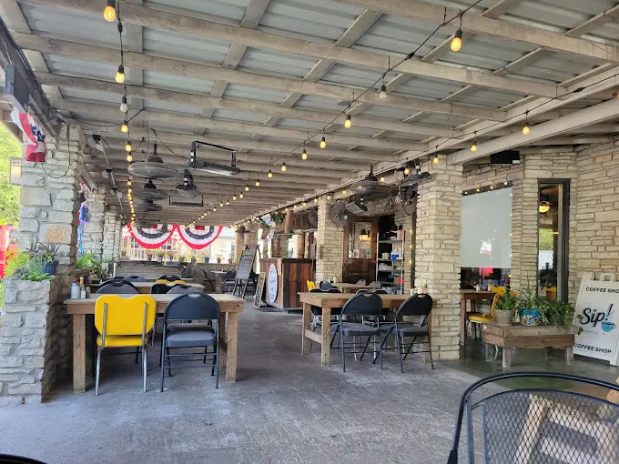 The Romantic Guide to Spoon Mountain Glamping for Beginners 13 Outdoor café with stone walls, string lights, various seating, and patriotic bunting. Tables and chairs are spread out, capturing the charm of Wimberley Café.